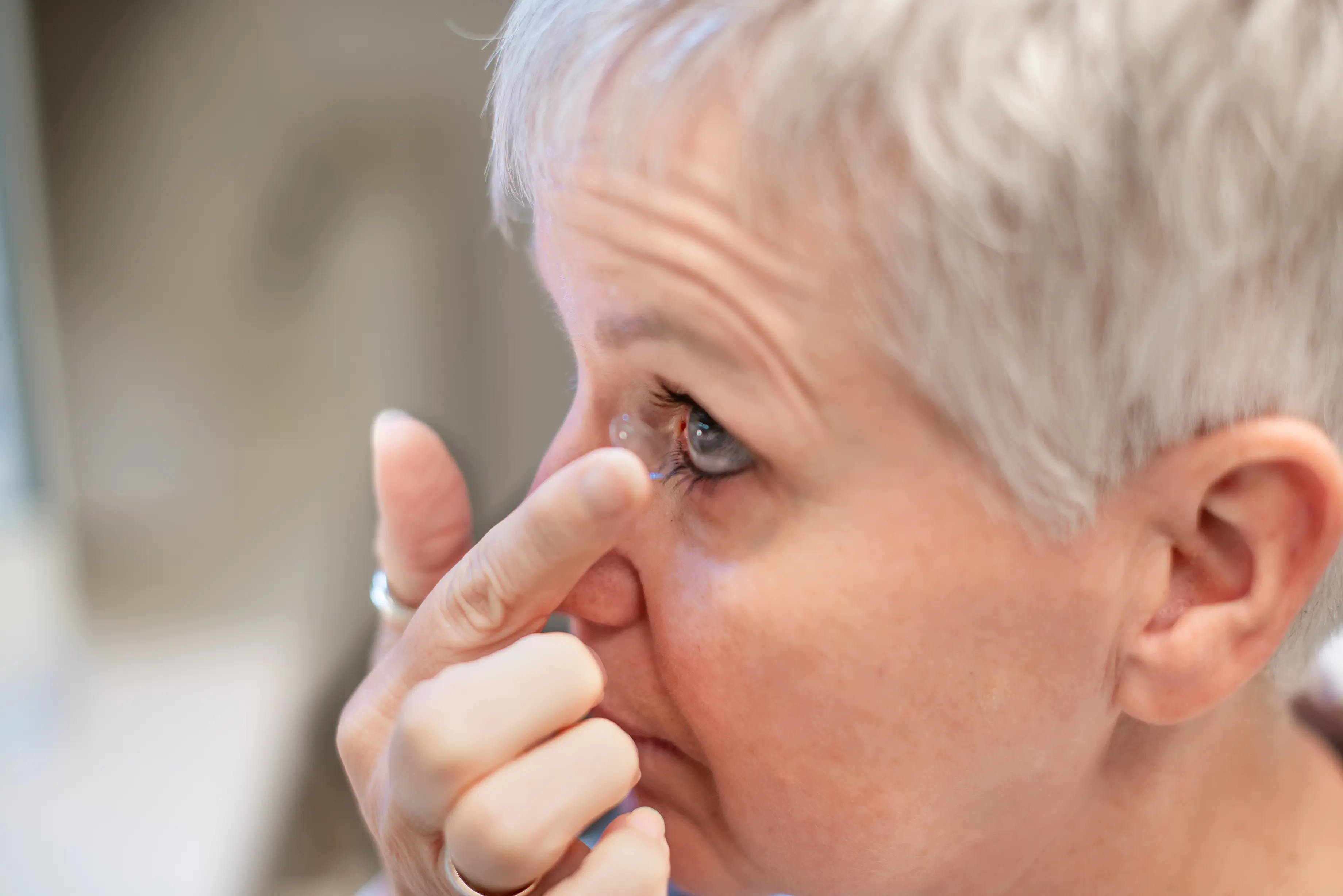 Frau hat eine Kontaktlinse auf dem Zeigefinger und führt diesen zu ihrem Auge.