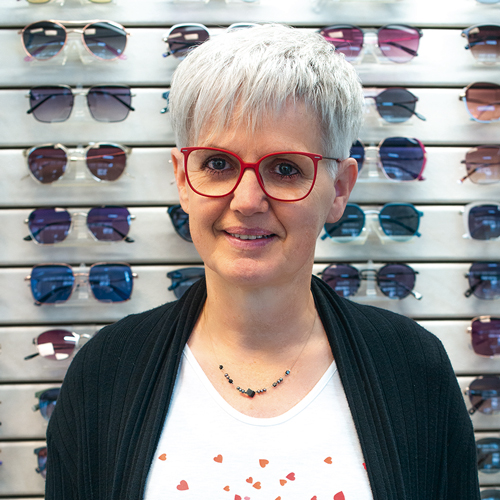 Mitarbeiterin mit kurzen weißen Haaren und einer roten Brillen.
